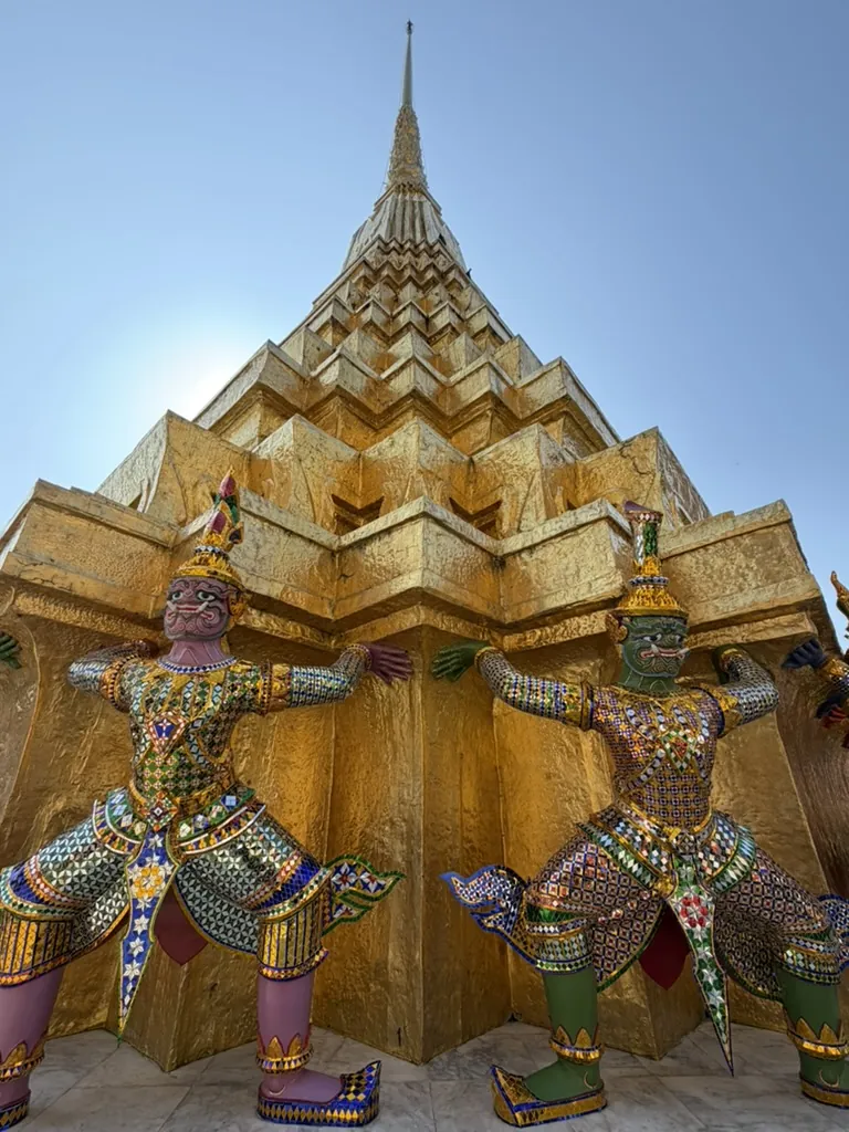 Colorful guardian figures beneath a golden chedi at Bangkok's Grand Palace